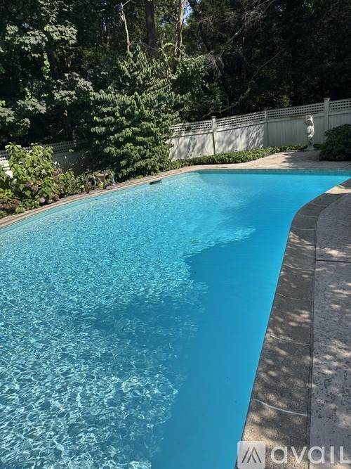 A swimming pool surrounded by a white fence and greenery.