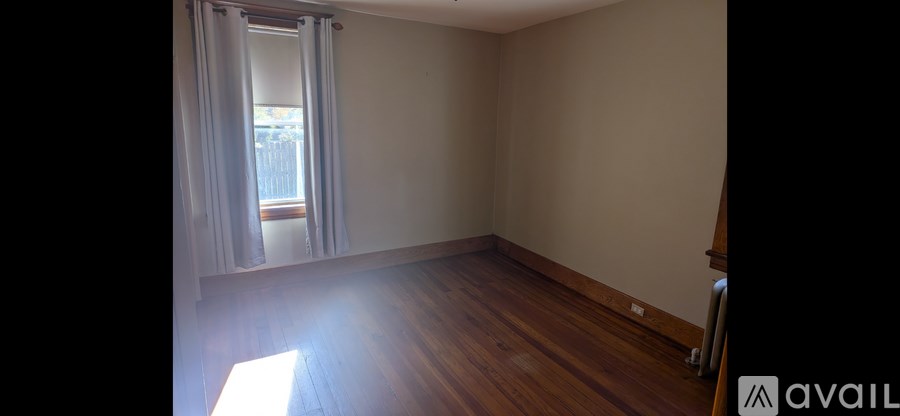 A room with wooden floors and a window with curtains.