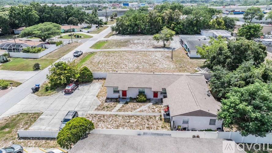 A large white building with a grey roof is surrounded by trees and other buildings.