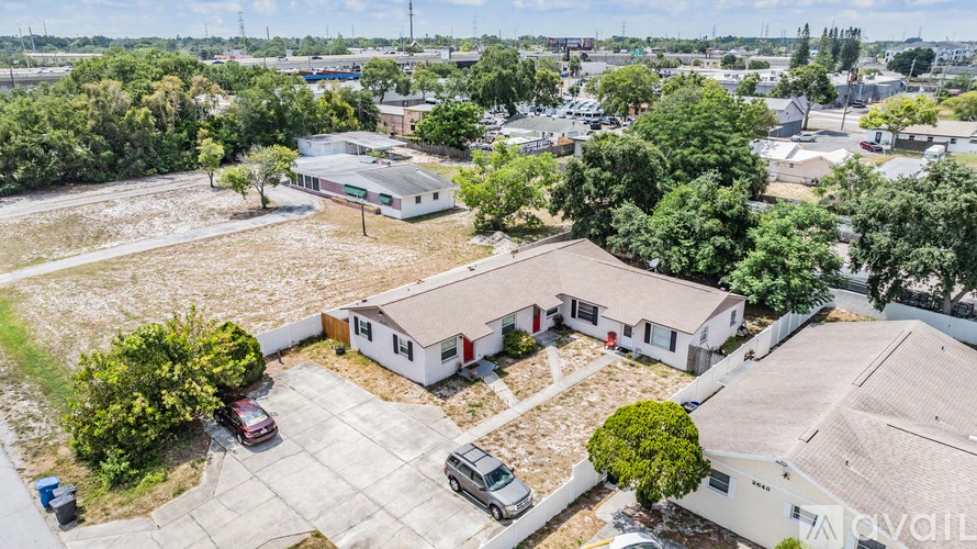 A large white building with a red roof is surrounded by trees and other buildings.