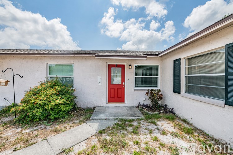 A white house with a red door and green bushes in front.