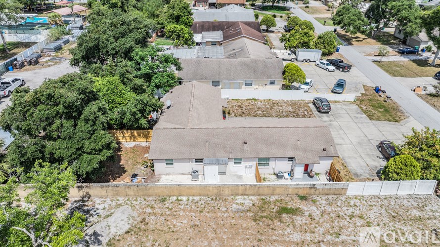 A large white building with a grey roof is surrounded by trees and a parking lot.