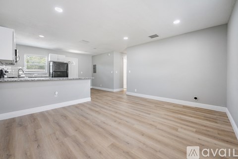 A spacious room with wooden flooring and a kitchen area with white appliances.