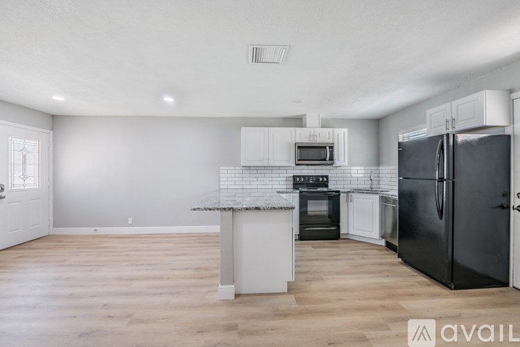 A kitchen with a black fridge, white cabinets, and a white island with a marble top.