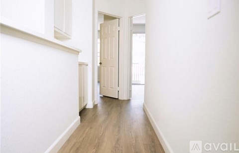 A hallway with a wooden floor and white walls leading to a door.