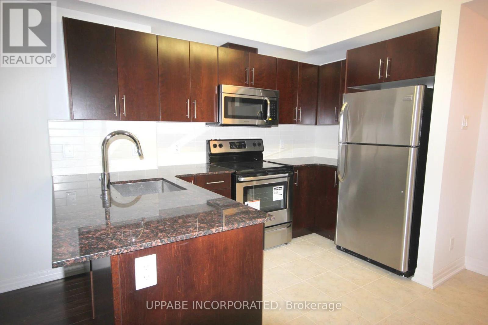 A kitchen with a refrigerator, microwave, oven, and sink.
