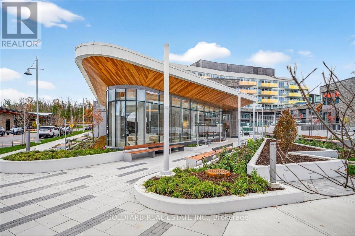 A modern building with a curved wooden roof and glass windows is surrounded by a landscaped area with benches and plants.
