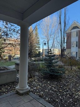 A white column stands on a porch with a view of a tree and a building in the background.