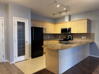 A kitchen with a black refrigerator and wooden cabinets.