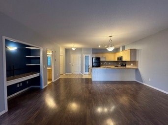 A spacious living room with hardwood floors and a kitchen area in the background.