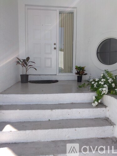 A white door with a window above it and a plant on the steps.