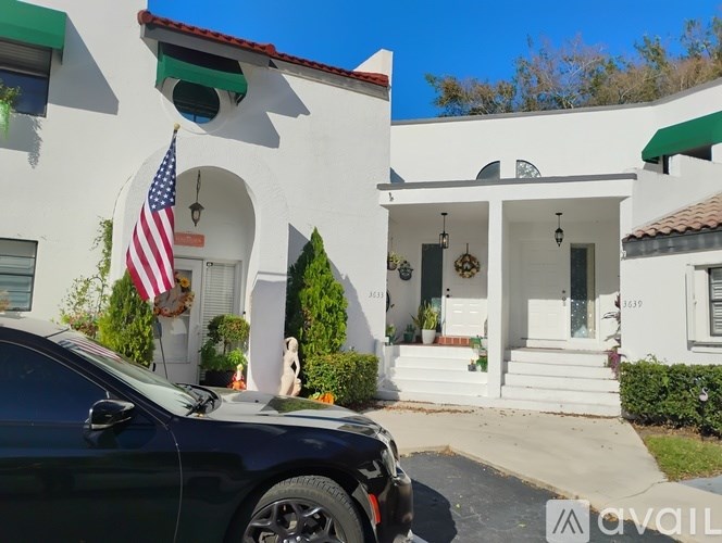 A black car is parked in front of a white house with a green awning.