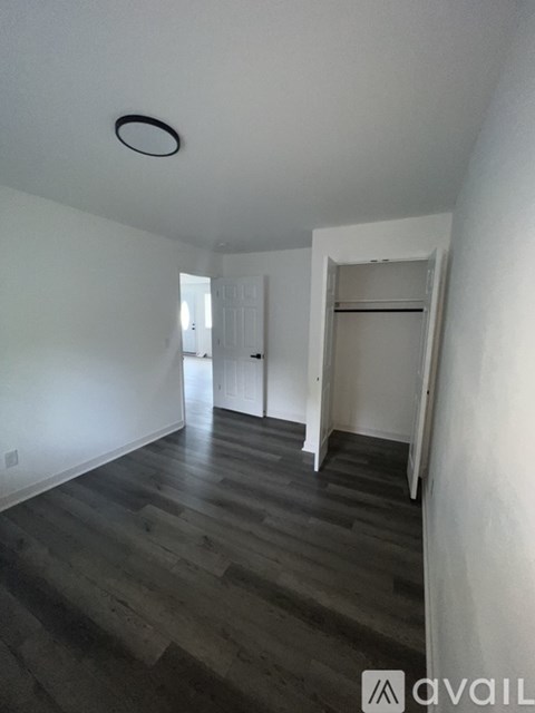 A room with wooden floors and white walls, with a doorway leading to another room.