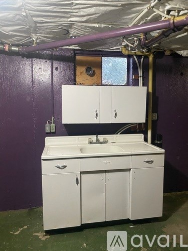 A white bathroom vanity with a sink and a cabinet is in a room with purple walls.