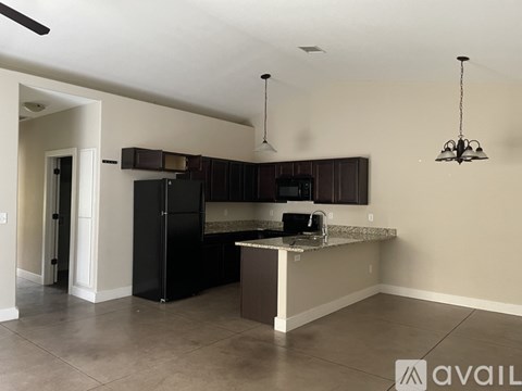 A kitchen with a black refrigerator and a countertop with a microwave.