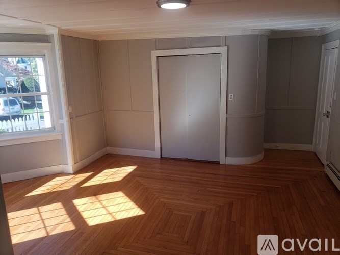 A room with wooden flooring and a large window letting in sunlight.