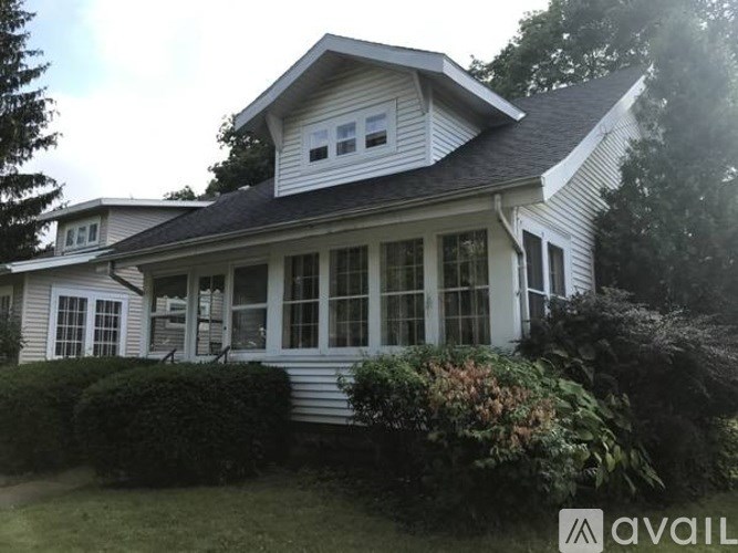 A house with a white facade and a grey roof is surrounded by greenery.
