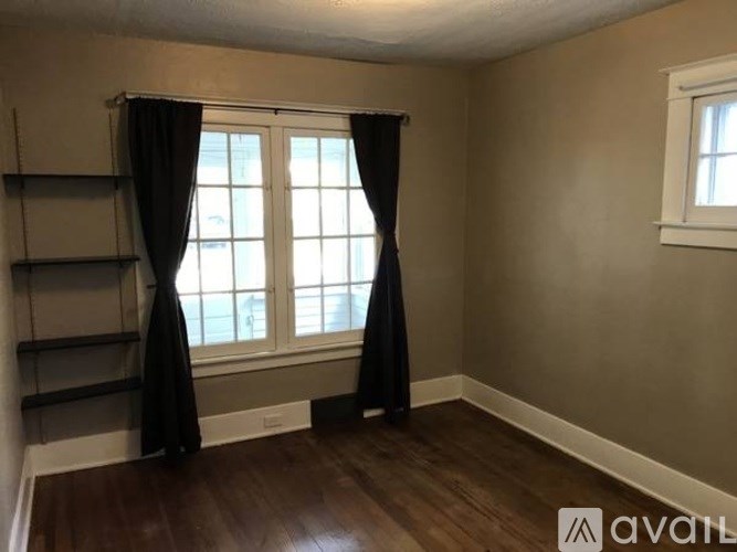 A room with a window, black curtains, and wooden flooring.