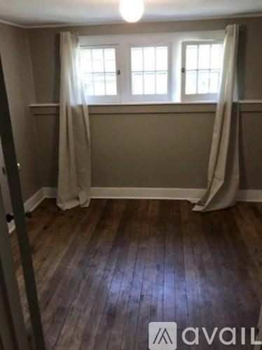 A room with wooden floors and a window with curtains.