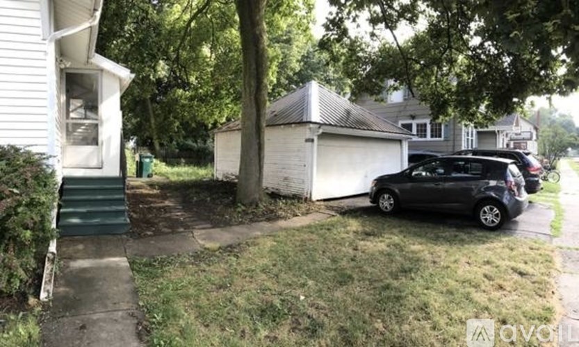 A black car is parked on a driveway in front of a white house.