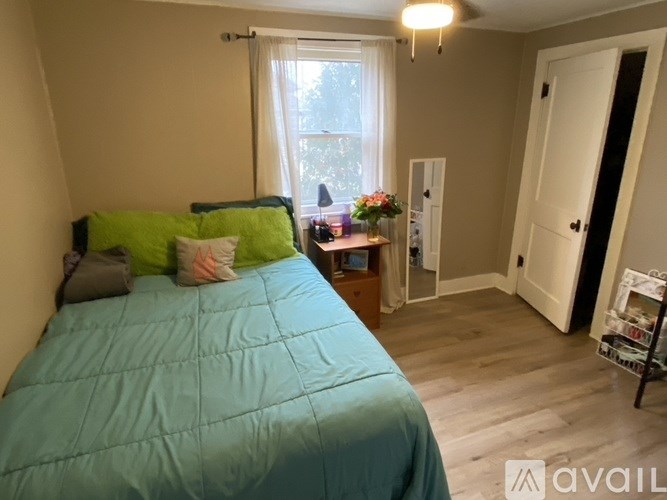 A bedroom with a blue comforter and a window with white curtains.