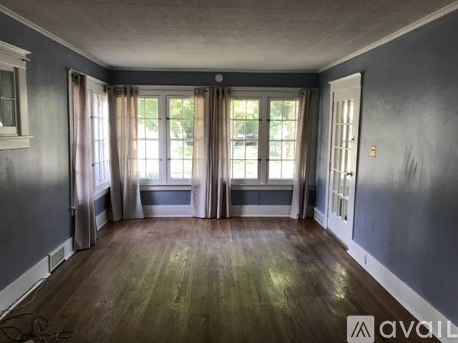 A room with wooden floors and a large window with curtains.