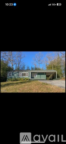 A house with a green roof and white walls is surrounded by trees.