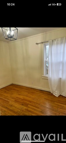 A room with wooden flooring and a window with white curtains.