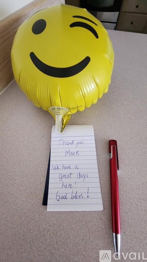A yellow balloon with a smiley face and a note saying "thank you Mark, we have a great day here, good luck!" is on a table.