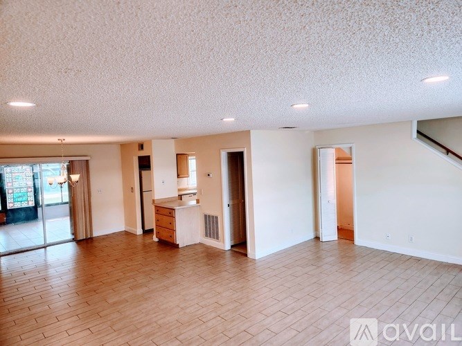 A spacious living room with hardwood floors and a kitchen area in the background.