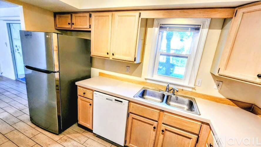 A kitchen with a black fridge, white dishwasher and wooden cabinets.
