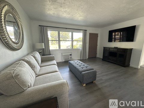 A living room with a grey couch and a round mirror on the wall.
