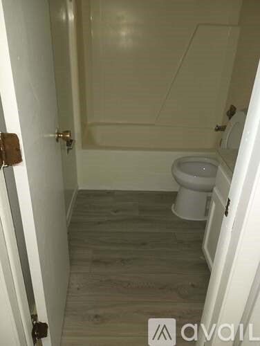 A white toilet in a small bathroom with wooden flooring and a white door.