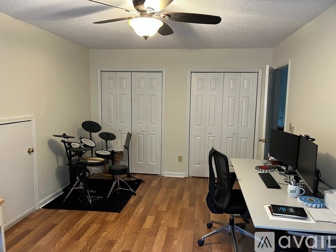 A room with a drum set and a desk with a computer.