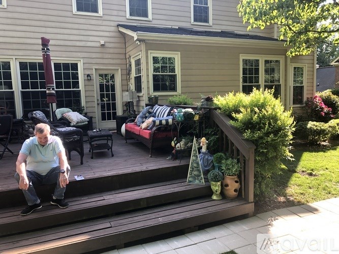 A man is sitting on a wooden deck outside a house.