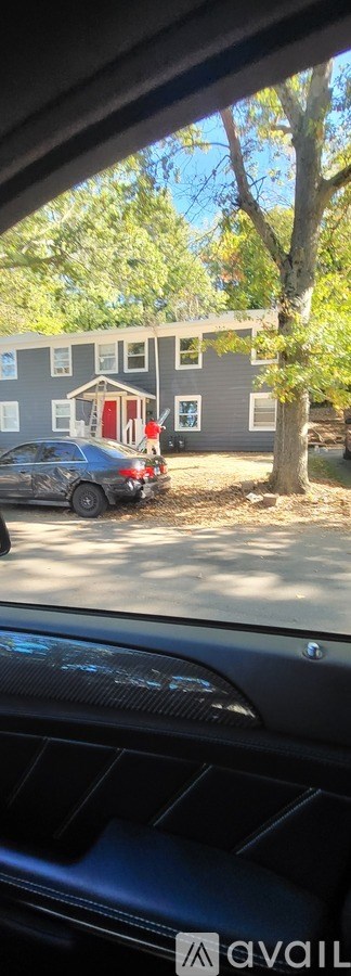 A car is parked in front of a grey house with a red door.