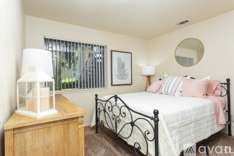 A bedroom with a white bed and a wooden nightstand with a white lamp on it.