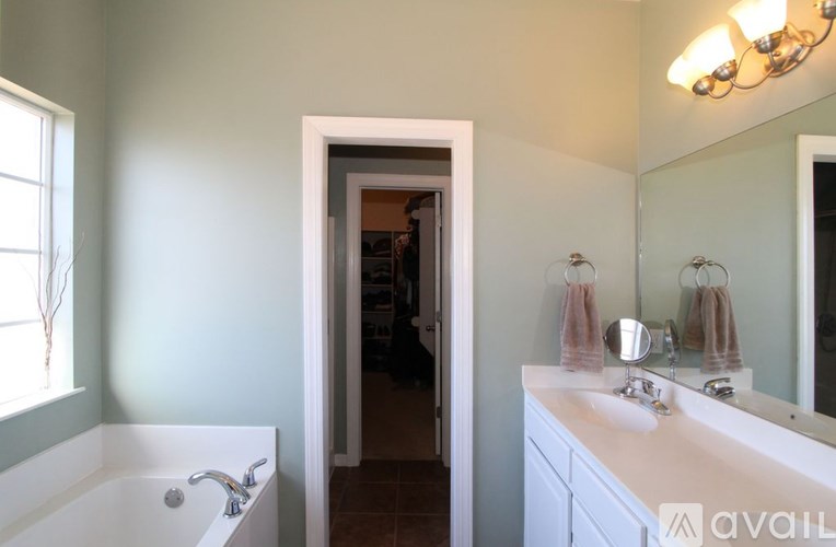 A bathroom with a white tub and sink, a mirror, and a chandelier.