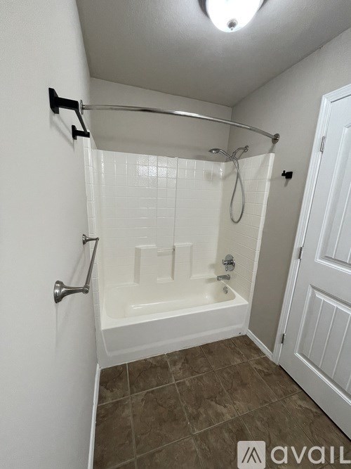 A bathroom with a white tub and brown tiles.