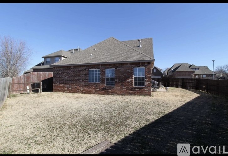 A house with a brown brick exterior and a grey roof is surrounded by a fence and has a grassy yard.