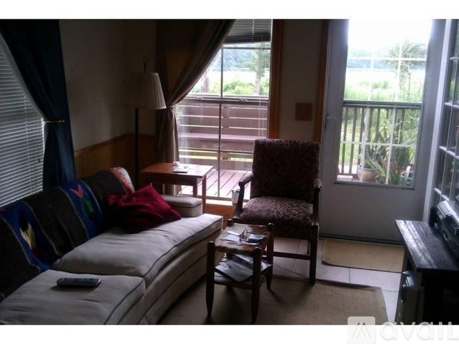 A living room with a sofa, chair, and a window overlooking a balcony.