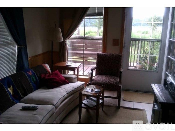 A living room with a sofa, chair, and a window overlooking a balcony.