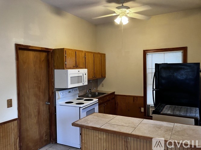 A kitchen with a white stove and microwave, wooden cabinets, and a black refrigerator.