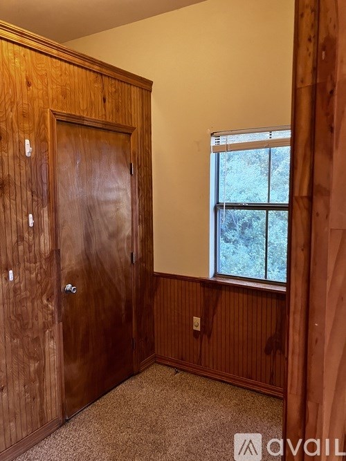 A room with a wooden door and a window with a view of trees outside.