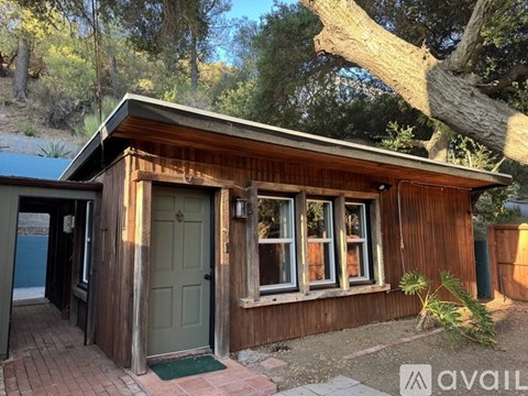A small wooden cabin with a green door and windows is surrounded by nature.