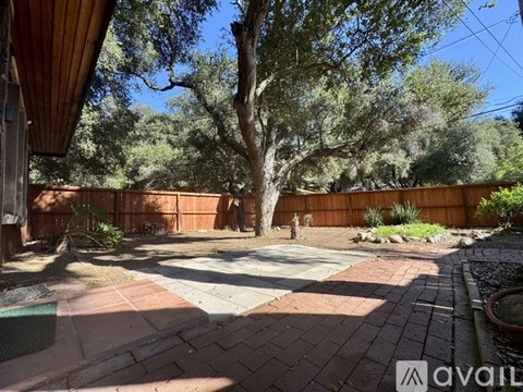 A backyard with a tree, a fence, and a brick patio.