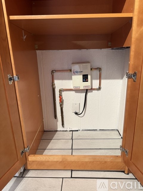 A small wooden cabinet with a white tile floor and a white wall with a pipe and valve.