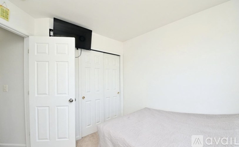 A bedroom with a bed, a door, and a wall-mounted TV.
