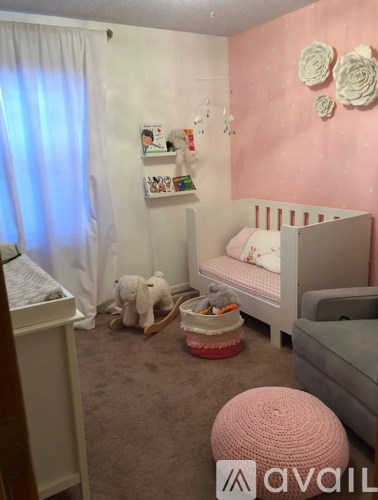 A baby's room with a white crib, a pink ottoman, and a white teddy bear.