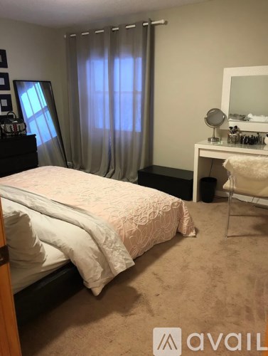 A bedroom with a bed, desk, chair, and window with curtains.